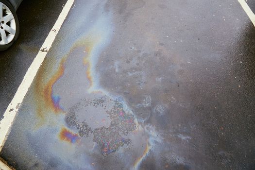 Colorful gas stain on wet asphalt. Oil stain caused by a leak under a car or truck.Environmental pollution concept.