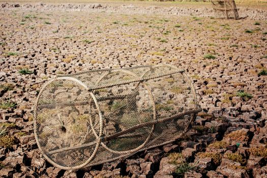 Fish trap device on arid soil of pond.