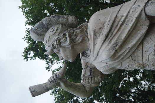 sculpture of classical water god blowing conch shell - ancient natural trumpet. Stone sculpture of a Triton, blowing on his conch shell trumpet.