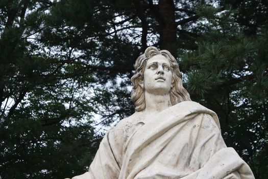 Statue of a man holding a book in one hand. White marble statue of man in a public park