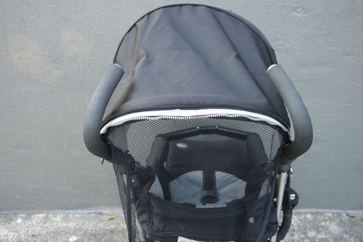 Black color baby stroller with head covering. Stroller is with concrete background