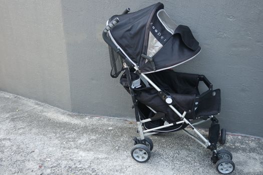 Black color baby stroller with head covering. Stroller is with concrete background