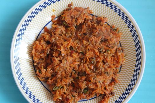 Top closeup view of a homemade dish made from carrot and vegetables served in a ceramic plate.