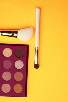 Eyeshadows and makeup brushes on a yellow background top view professional cosmetics. High quality photo