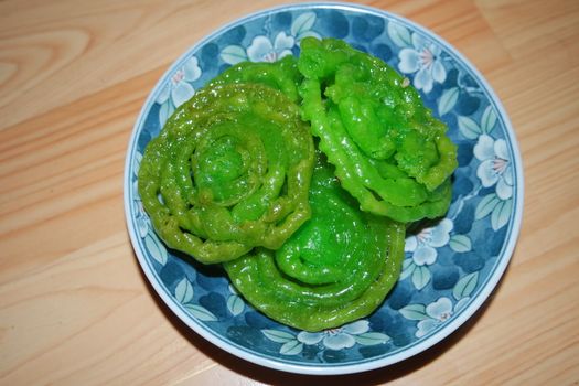 Crispy sweet Asian dessert green Jalebi cooked and served in ceramic plate, Indian sweet street food with juicy syrup, a closeup view.