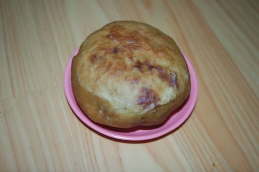 Closeup view of homemade tasty potato bread rolls bun placed in a pink plastic plate over wooden floor.