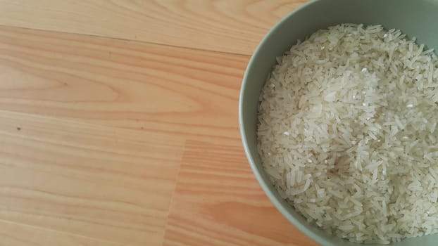 Top closeup view of heap of rice in a ceramic bowl placed over wooden floor.