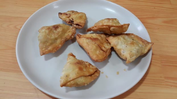 Closeup of delicious home made spicy and crunchy samosa pastries placed in a white ceramic plate on wooden floor