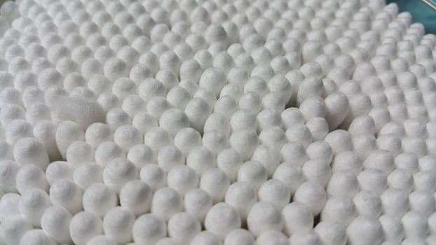 Closeup view of several cotton buds heads arranged in rows and columns. The cotton buds consist of one small wad of cotton wrapped around one or both ends of a short rod made of wood or plastic.