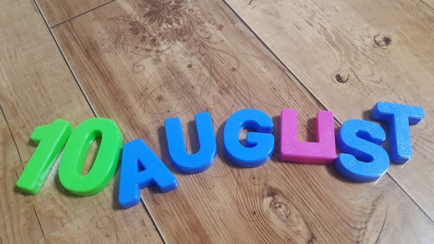 Plastic colored alphabets making words 10 August are placed on a wooden floor. These plastic letters can be used for teaching kids.