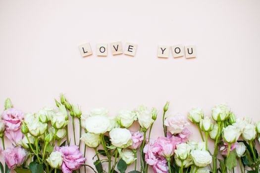 Inscription of wooden blocks love you. Delicate touching bouquet of white and pink flowers on a light pink background. Layout. Flat lay