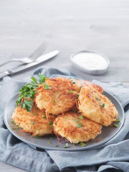 Close up view of potato pancakes. Potato flapjack on gray plate over gray wooden table, with fresh parsley and sour cream. Copy space for text. Vertical.