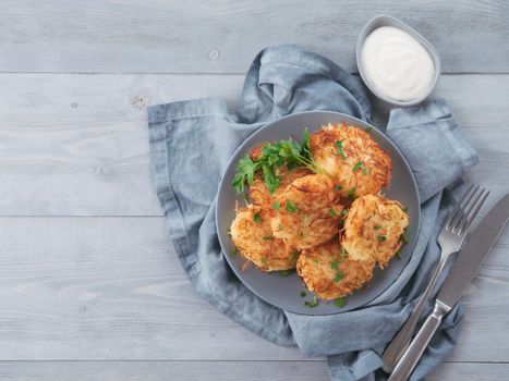Close up view of potato pancakes. Potato flapjack on gray plate over gray wooden table, with fresh parsley and sour cream. Copy space for text. Top view or flat-lay.
