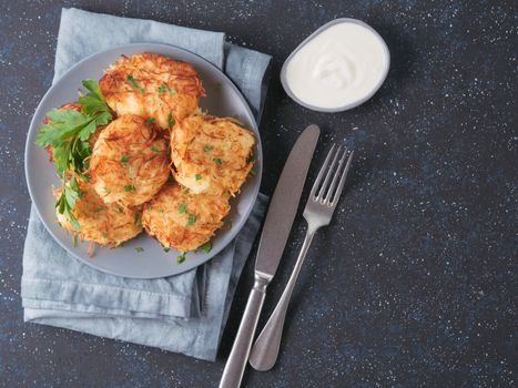Close up view of potato pancakes. Potato flapjack on gray plate over dark blue background, with fresh parsley and sour cream. Copy space for text. Top view or flat-lay.