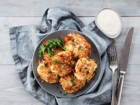 Close up view of potato pancakes. Potato flapjack on gray plate over gray wooden table, with fresh parsley and sour cream. Copy space for text. Top view or flat-lay.