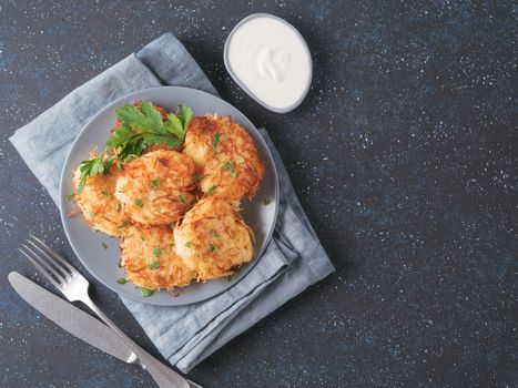 Close up view of potato pancakes. Potato flapjack on gray plate over dark blue background, with fresh parsley and sour cream. Copy space for text. Top view or flat-lay.