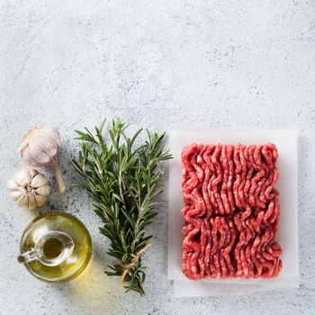 Fresh raw minced beef, fresh rosemary, garlic, olive oil on light gray cement background with copy space. Top view or flat lay. Cooking ingredients concept. Square shape