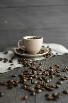 Coffee cup filled of fresh arabica or robusta coffee beans with scattered coffee beans on a linen textile and wood table