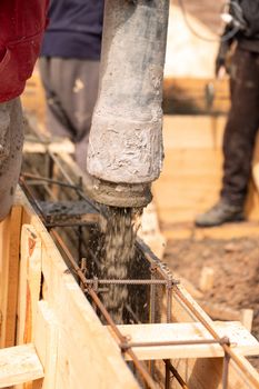 Close up of construction worker laying cement or concrete into the foundation formwork with automatic pump. Building house foundation