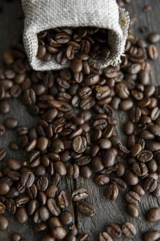 Coffee beans scattered from a linen bag on a wooden table. Fresh roasted arabica coffee beans