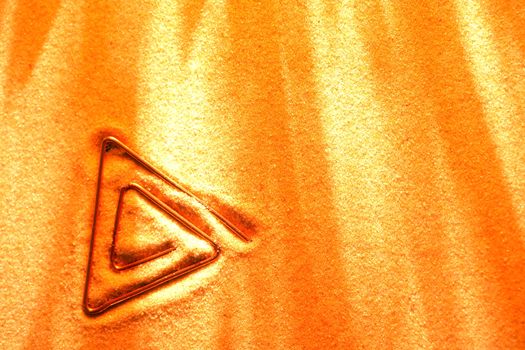 Abstract triangular symbol made from copper wire on sand surface