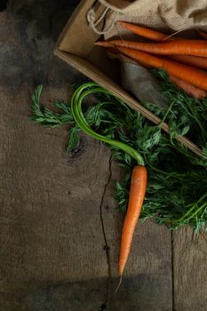 Fresh organic carrots in a box with canvas on antique wooden table. Rustic kitchen concept. Banner, poster, mock up. Grunge, vintage, rustic style