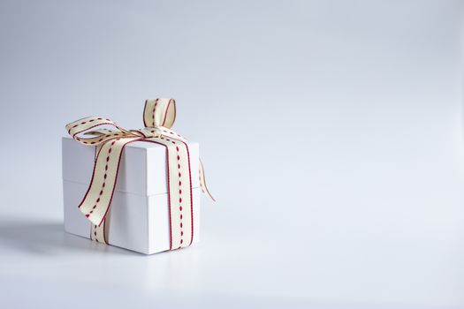 Small white gift box with dotted red and whote ribbon on white background. greetings, Valentines, anniversary, Morhtes, wedding, birthday concept