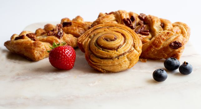 selection of French, Danish pastries with summer fruits on white marble background. Breakfast, morning treat, continental cafe