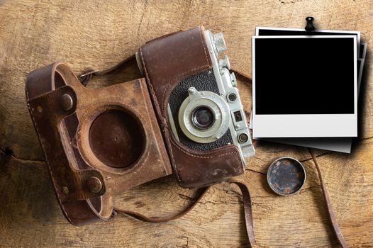 Ancient old vintage film camera with old lether cover and polatroid frames on brown old wood background. Flat lay, close up. Antique, vintage, grunge, classic concept. Mock up