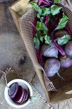 Bunch of fresh, spring, organic vegetables in a garden wooden box, with slices of beetroot in ceramic plate on old wooden background. Top view. Rustic, dramatic, organic kitchen. Ingredients, menu. Healthy life concept