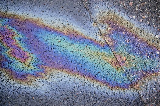 Gas stain on wet asphalt caused by a leak under a car or truck, abstract background