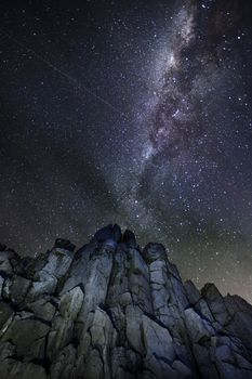 Views of night sky from below the tall rocky cliffs and light wispy cloud moves gently across the sky