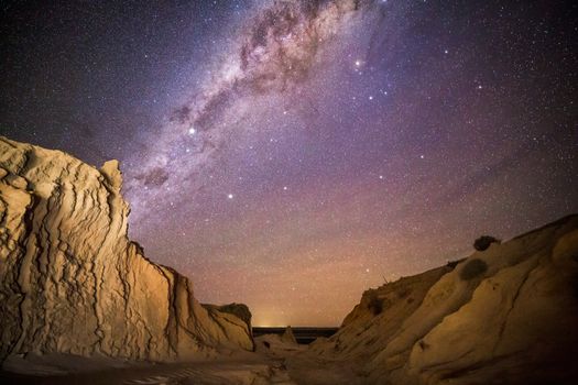 Night skies over desert landscape.  Milky way shining vividly overhead and a warm glow from nearby township in the far distance.  the textures of the desert are highlighted with a hand light.