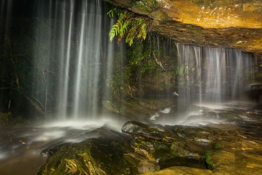 Waterfall tumbles over the cave roof at night, wies from inside the cave  with waterfall and cave illuminated by lights