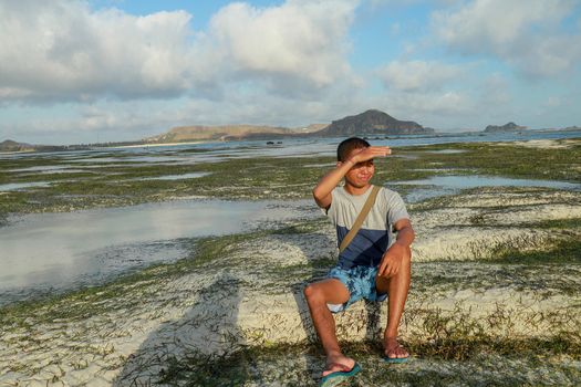 Portrait of an attractive young man on a tropical beach. Outdoor fashion portrait of handsome asian man at amazing tropical beach, in nice sunny day. Teenager with blue shorts and t-shirt.