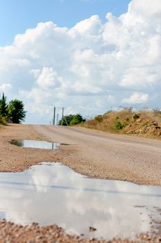 Puddles the next after the rain in the pits on the road. Clear weather.