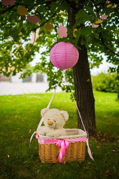 street decorations for a children's party. A basket with a teddy bear in a air balloon in a green park.
