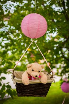 street decorations for a children's party. A basket with a teddy bear in a air balloon in a green park.