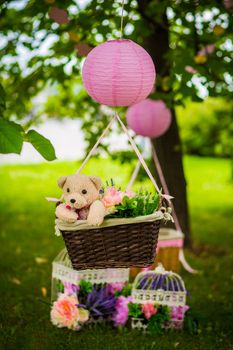 street decorations for a children's party. A basket with a teddy bear in a air balloon in a green park.