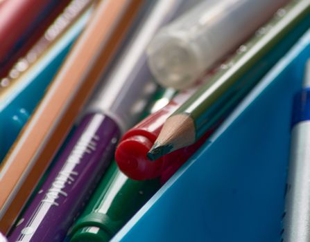 Sharp pencils and markers in red, green, blue and purple untidy and misplaced inside a craft box
