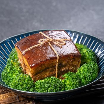 Dong Po Rou (Dongpo pork meat) in a beautiful plate with green vegetable, traditional festive food for Chinese new year cuisine meal, close up.