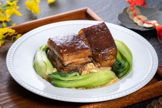 Dong Po Rou (Dongpo pork meat) in a beautiful plate with green vegetable, traditional festive food for Chinese new year cuisine meal, close up.