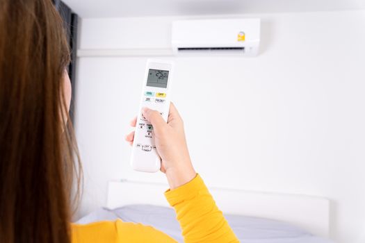 Woman is using white remote of air conditioner for turn on or adjust temperature of air conditioner inside the room.