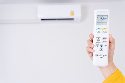 Human hand is using white remote of air conditioner for turn on or adjust temperature of air conditioner inside the room.