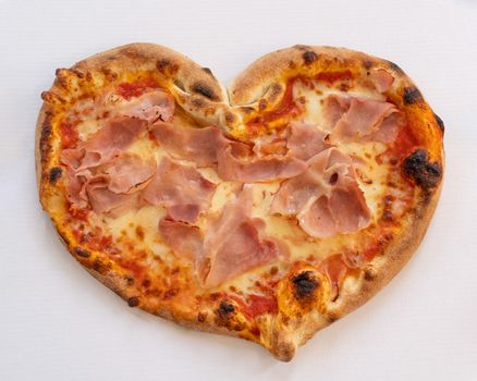 Heart shaped pizza with tomatoes and ham for Valentines Day on white cardboard background,Food concept of romantic love