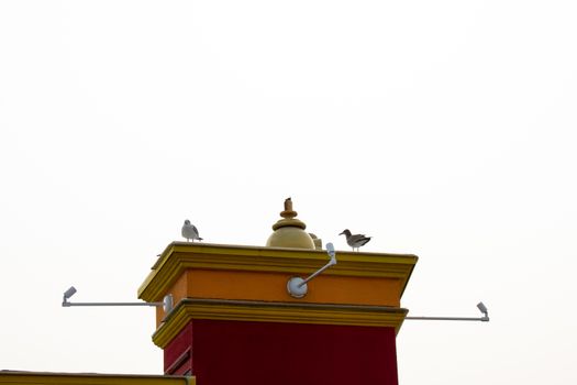 A Colorful Tower On a Building With Two Seagulls Sitting on it