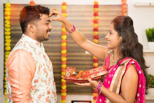 Woman applying Thilaka or Mark to his partner or husband's forehead during Karwa Chauth festival celebration while both in traditional dress