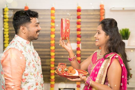 Indian woman in traditional dress seeing her husband or partner through sieve during Hindu Indian religious karwa chauth festival at home