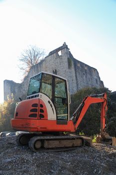 Small excavator on a consruction site hill in front of an ancient castle ruin