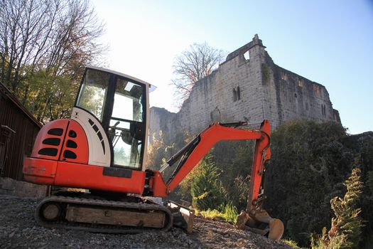 Small excavator on a consruction site hill in front of an ancient castle ruin